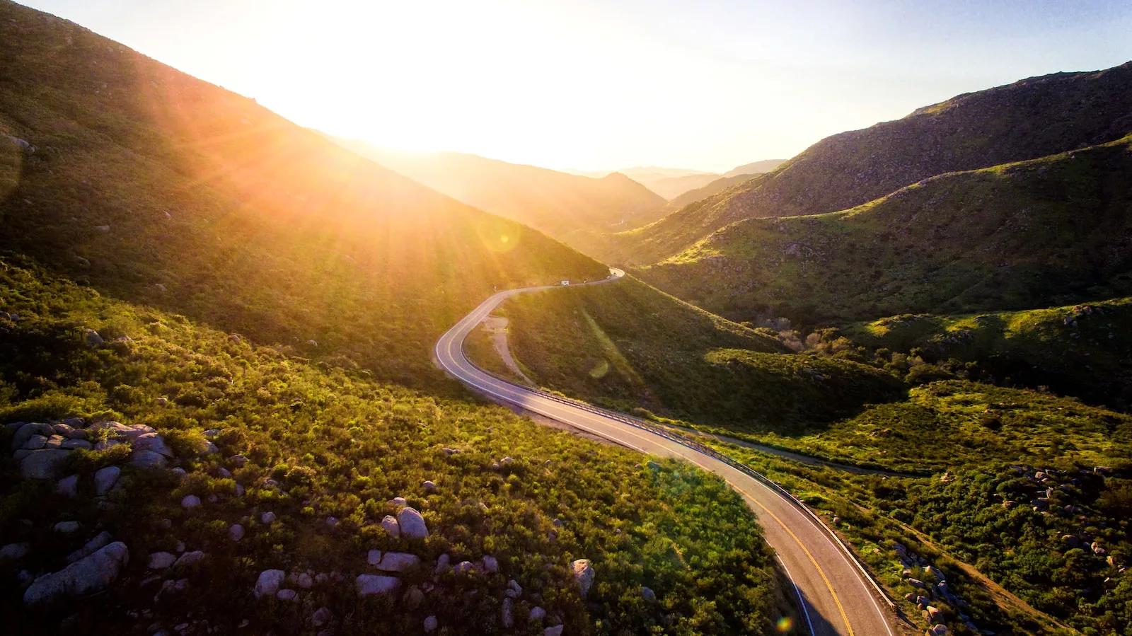 A winding road through mountains, illuminated by the warm hues of a sunset sky.