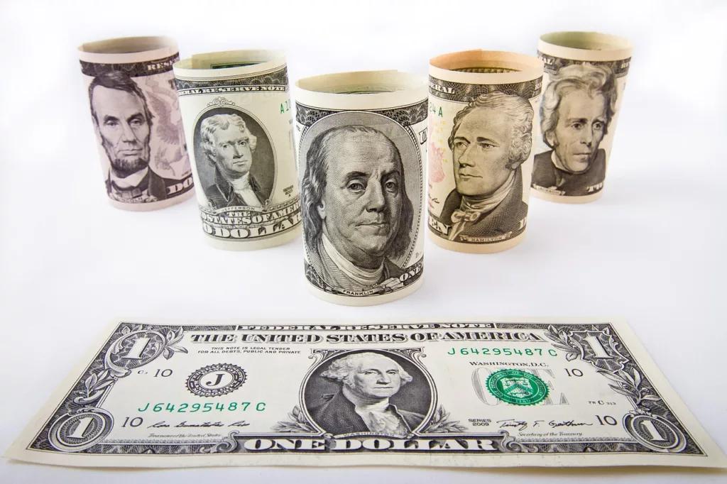 Several rolls of currency arranged with a dollar bill on a table