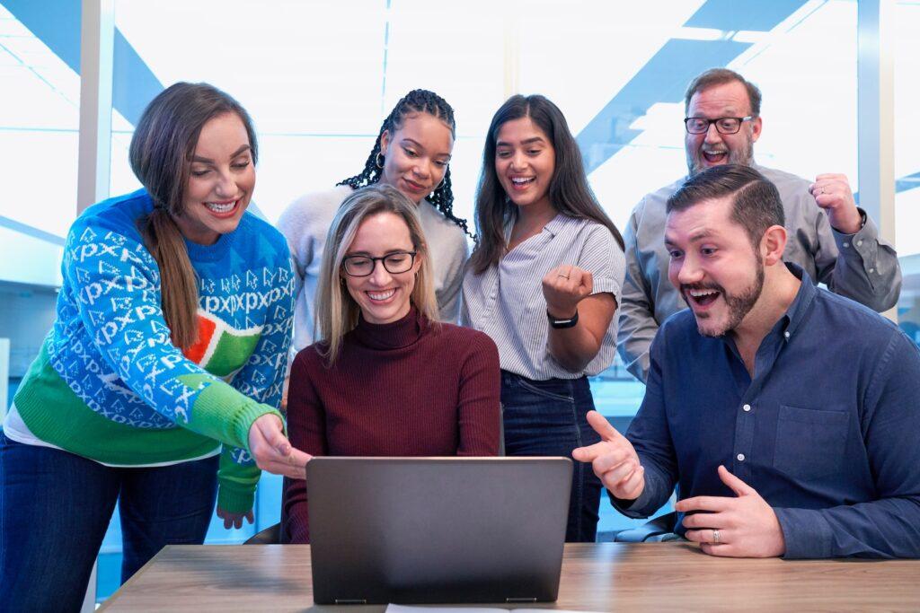 A diverse group of people smiling and pointing at a laptop