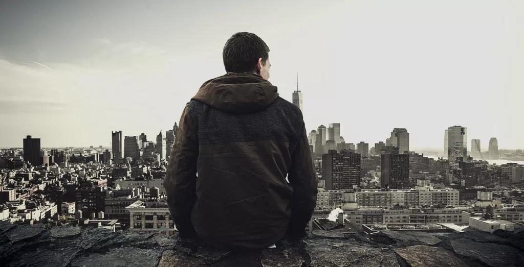 A man sits on a ledge, gazing out over a sprawling cityscape