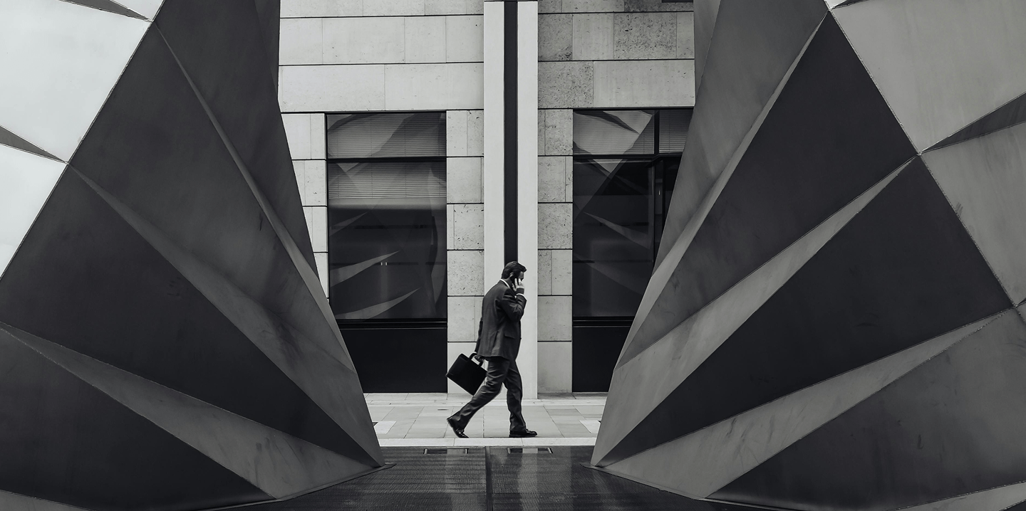 businessman walking next to modern art sculpture while on phone