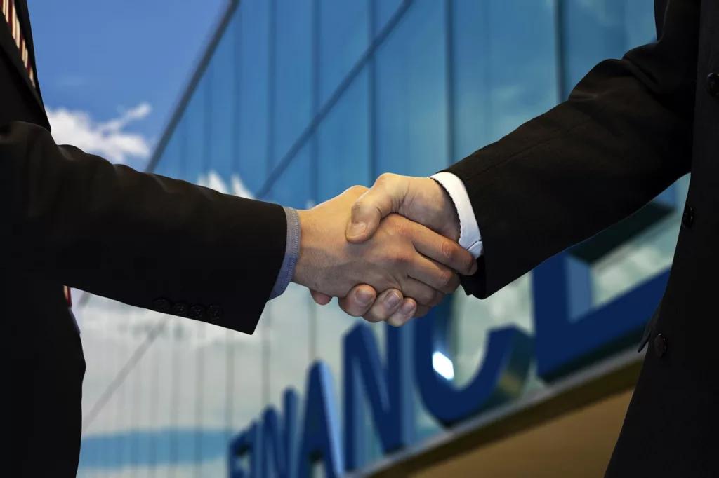 Two business professionals shaking hands in front of a modern finance building