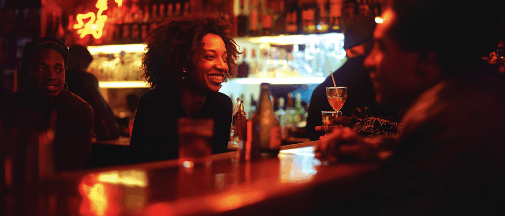 A lively bar scene with friends enjoying drinks and conversation in warm, dim lighting.