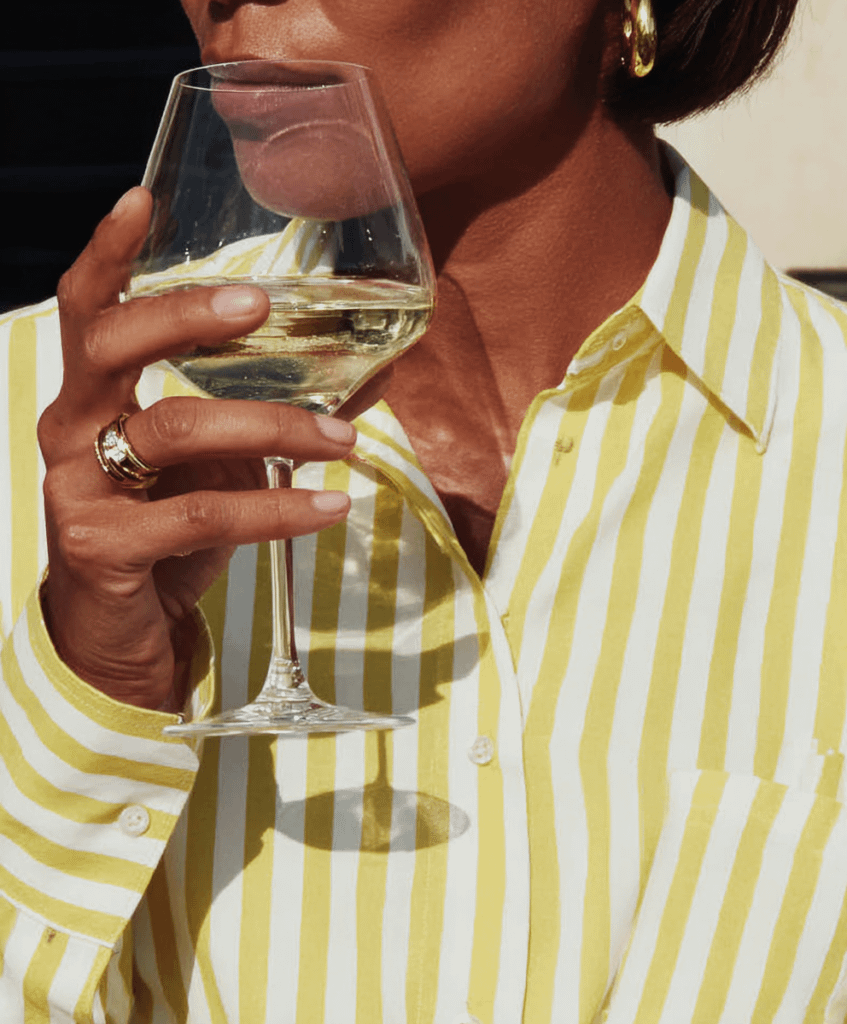 Close-up of a person in a yellow striped shirt holding a glass of white wine, showcasing elegant details and warm lighting.